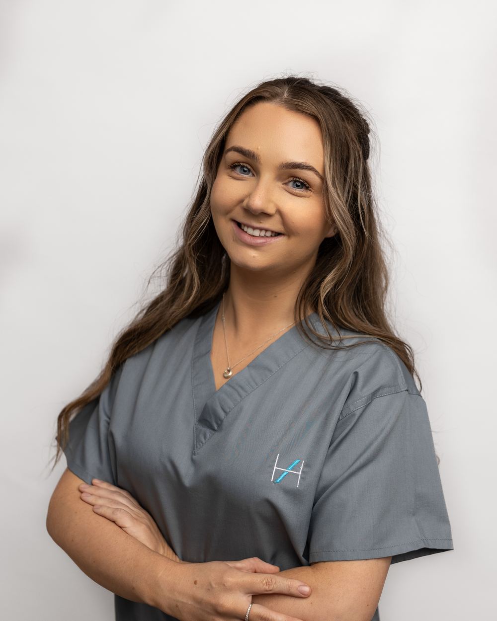 Georgina White in grey scrubs, smiling with her arms folded